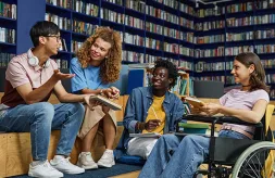 A diverse group of four students, including a young woman in a wheelchair, gathered in a college library and enjoying discussion