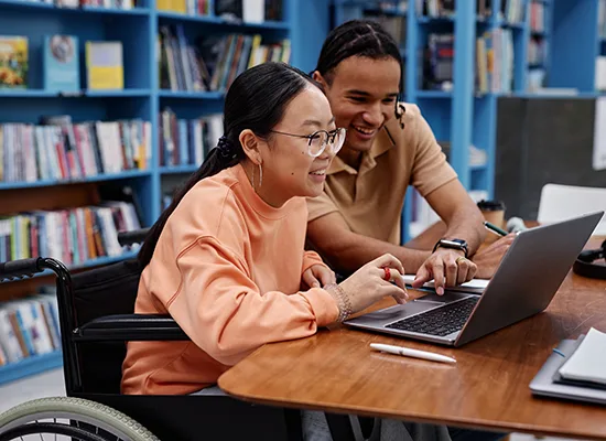 Side view portrait of smiling teenage girl with disability studying in college and using laptop with friend