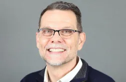 Headshot of Todd Williams. He has a light complexion, short brown hair and green eyes. He is wearing glasses, a white shirt with a collar and a navy, zip-up sweater.