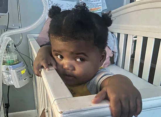 DSCC participant Kaharri Pittman, who is enrolled in the Home Care Program, sits inside his crib next to his ventilator