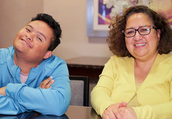 A mother and son smile together at a conference table.