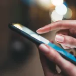 A close-up of dark-skinned hands holding a cell phone and touching the screen