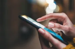A close-up of dark-skinned hands holding a cell phone and touching the screen
