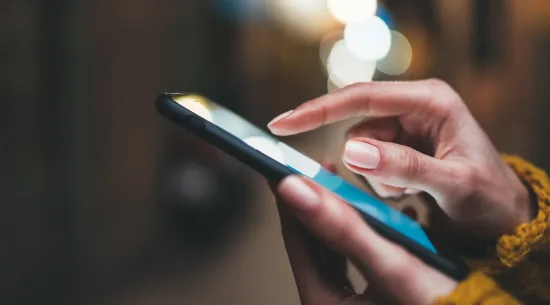 A close-up of dark-skinned hands holding a cell phone and touching the screen